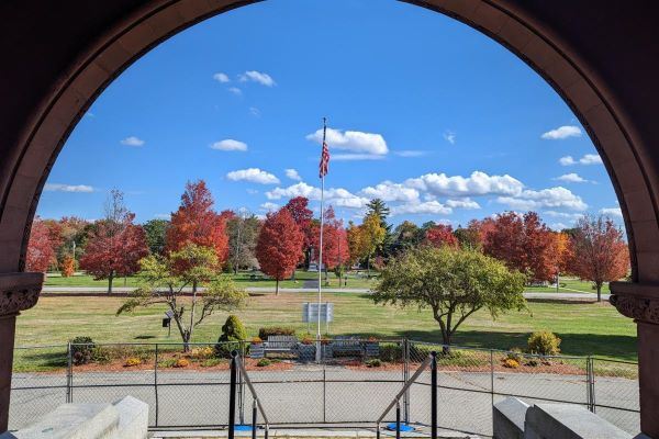 An archway opens onto a park with a flag and trees whose leaves have turned red.