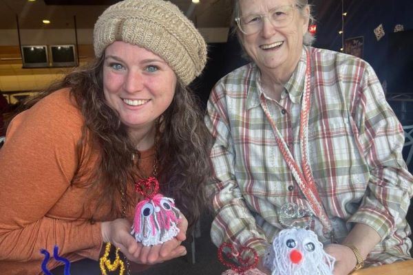 A senior and a young woman in a knitted hat show off a pair of whimsical yarn creatures.